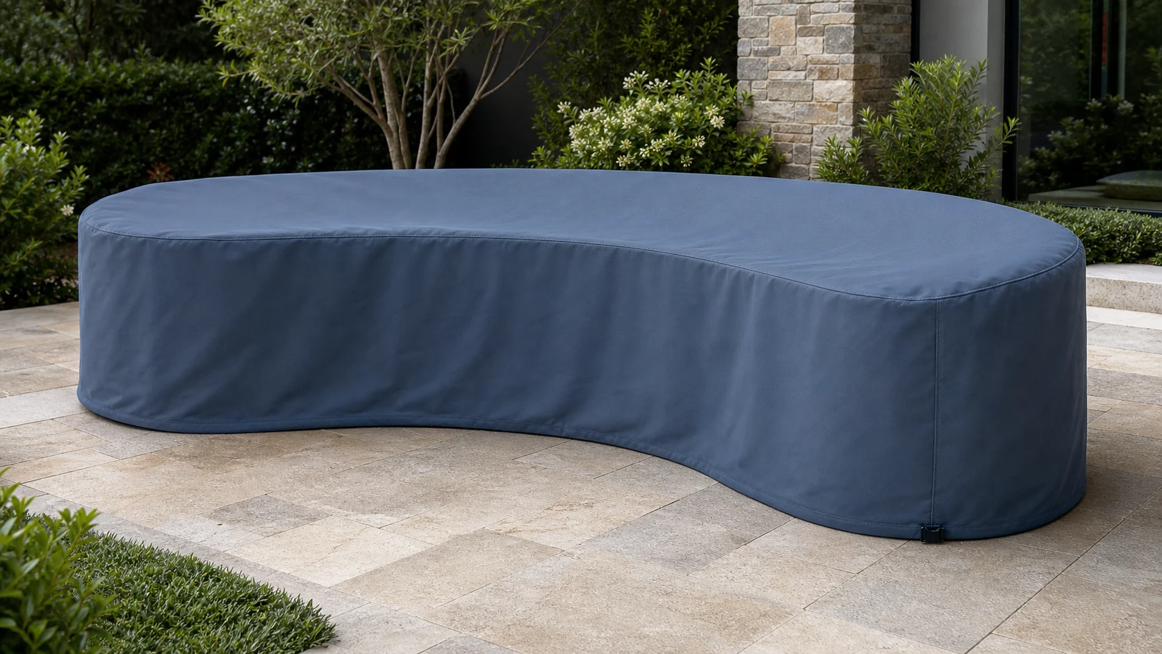 Slate blue fitted cover following the full crescent curve and rounded ends of an outdoor sofa on a landscaped patio